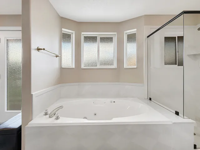 Built-in soaking tub with chrome fixtures, surrounded by white paneling, and a separate glass-enclosed shower