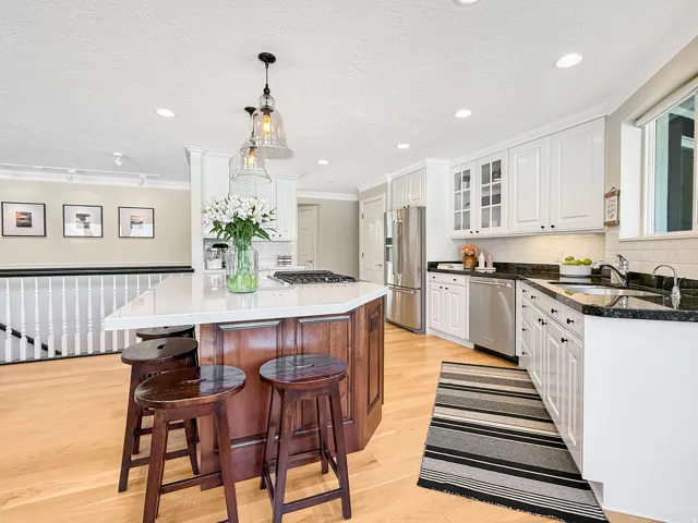 Kitchen featuring a central island with white countertop, light wood-finish flooring, white cabinetry, dark countertops, and stainless steel appliances