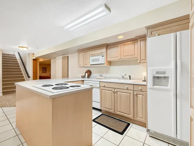 Kitchen featuring an electric range cooktop on an island, light wood-finish cabinetry, white appliances, and tiled flooring