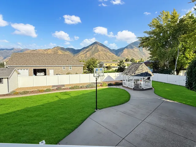 Expansive concrete patio with a white gazebo, lush green lawn, and a white privacy fence