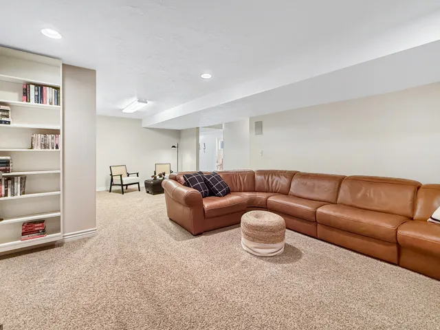 Spacious basement recreation room featuring a curved cognac leather sectional, neutral carpet flooring, and recessed ceiling lighting