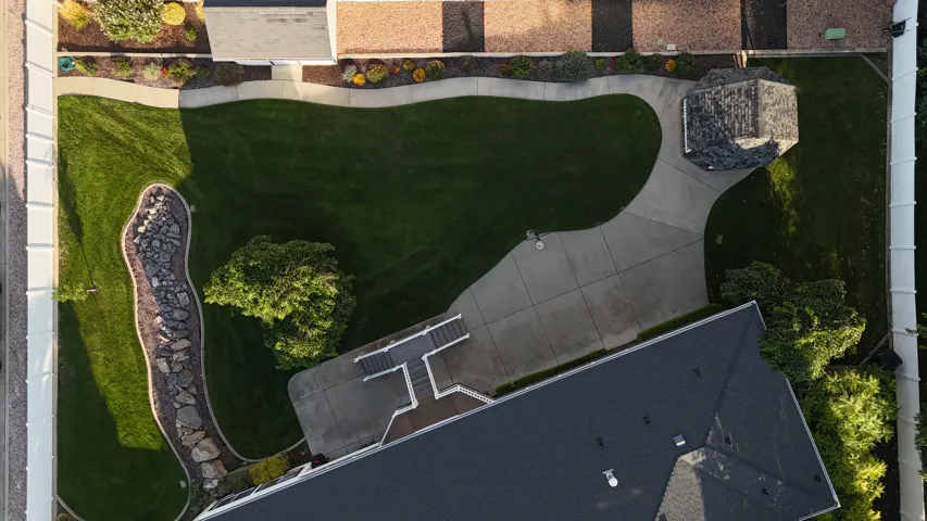 Expansive backyard featuring a manicured lawn, established landscaping, concrete pathways, and a detached gazebo with a shingled roof