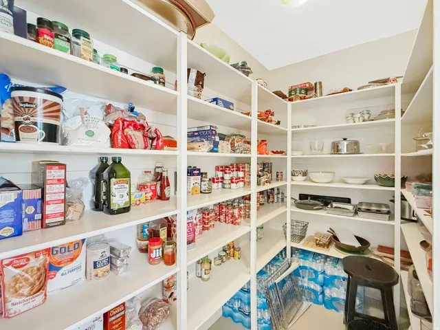 Spacious pantry featuring floor-to-ceiling white cabinetry with multiple shelves for organized storage, ample capacity for pantry staples and kitchenware, and tile flooring throughout