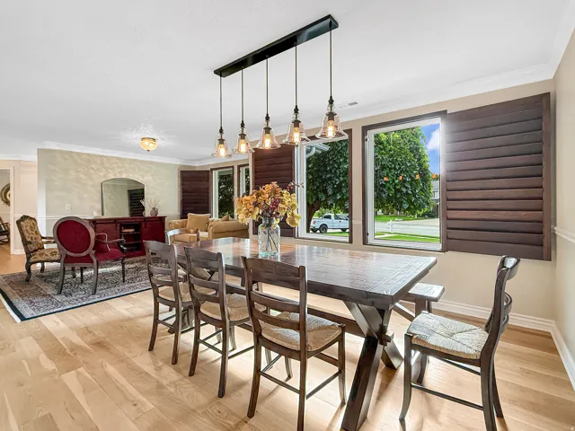 Open-concept dining area featuring wood-finish flooring, a linear pendant light fixture, and window shutters
