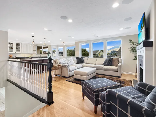 Hardwood flooring throughout, recessed lighting, white kitchen cabinetry with dark countertops, a fireplace with a mantel, and multiple windows providing natural light