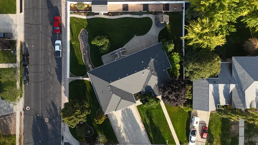 Gable roofline, expansive green lawn, paved driveway, mature trees, and a decorative stone-lined landscaping feature
