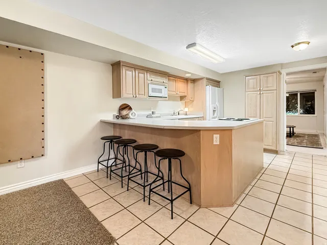 Kitchen with light wood-finish cabinetry, white countertops, built-in microwave, and tile flooring