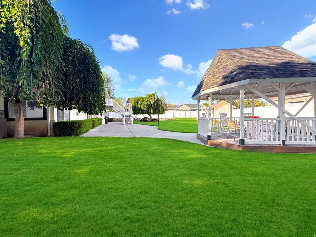 Expansive green lawn, white gazebo with shingle roof, concrete patio, mature trees, and privacy fencing