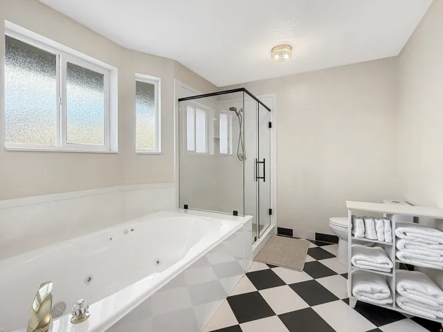 Soaking tub with checkerboard surround, walk-in shower with clear glass enclosure, and black and white checkered flooring