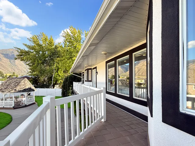 Exterior featuring a covered walkway with white railing, stucco siding, dark-framed windows, and a detached gazebo with a shingled roof