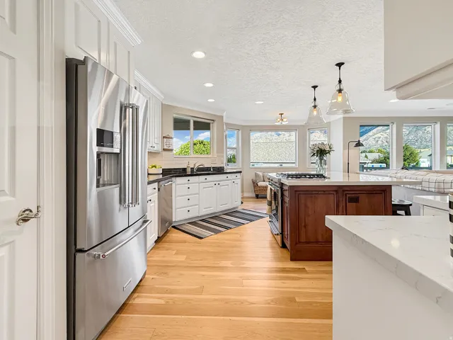 Gourmet kitchen featuring stainless steel appliances, light wood-finish flooring, white cabinetry, dark stone countertops, and a wood-paneled kitchen island with pendant lighting