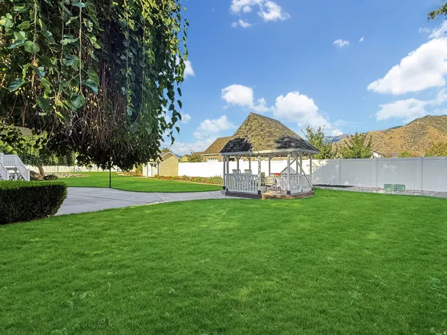 Gable roof gazebo with a shingle roof, surrounded by a lush lawn and a white privacy fence