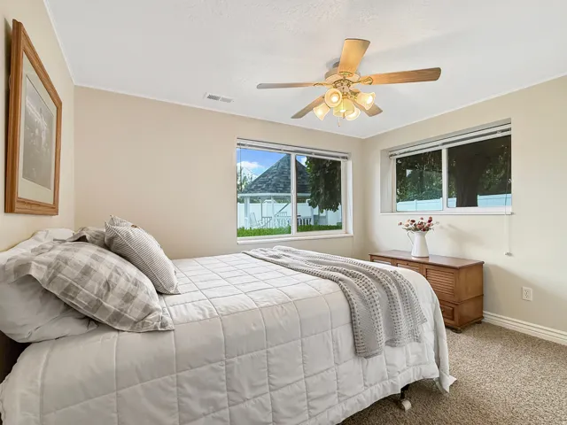 Neutral-toned walls, two windows with white trim, a ceiling fan with light fixture, and textured carpeting