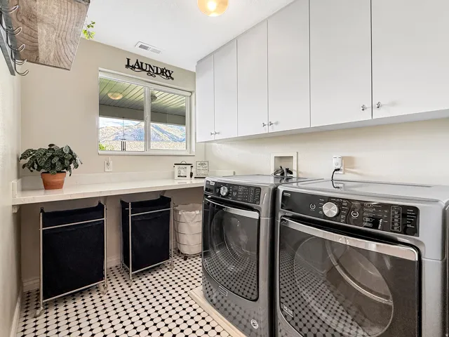 White upper cabinetry, extensive countertop space, window, and black-and-white patterned tile flooring