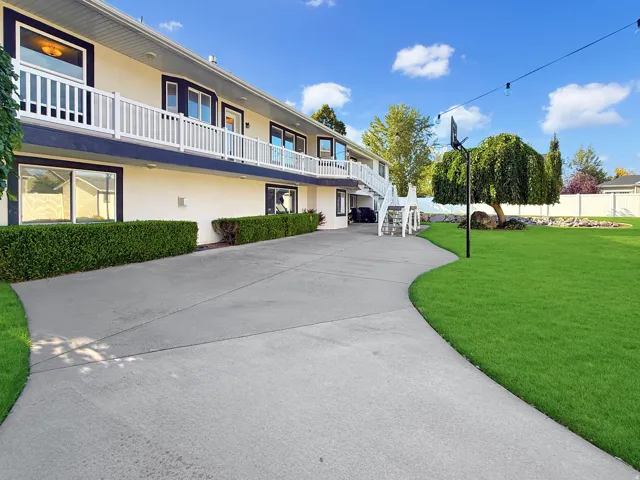 Expansive rear exterior with a full-length upper-level balcony, lower-level patios, a wide concrete path, and a lush green lawn