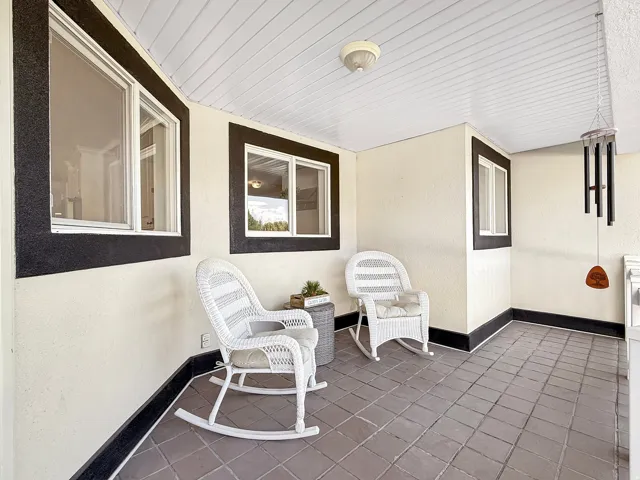 Covered porch with square tile flooring, textured walls, and white framed windows