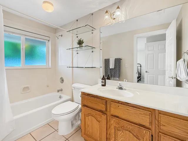 Bathroom featuring a full vanity with wood cabinetry, a large wall-mounted mirror, a tub-shower combination, and tiled flooring