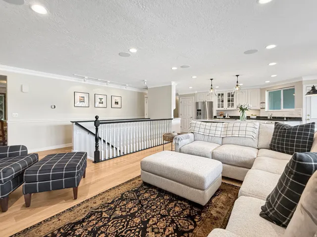 Recessed lighting throughout, crown molding, wood-finish flooring, white kitchen cabinetry, and black railing with white balusters