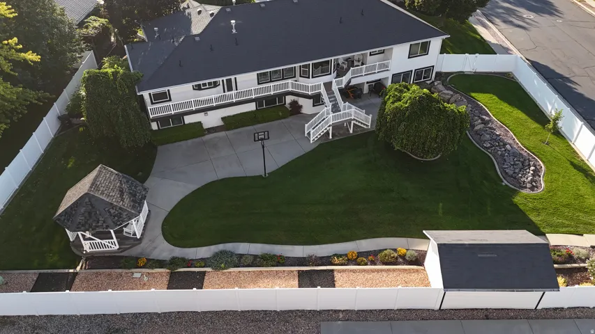 Expansive green lawn, white picket fence, paved driveway, detached gazebo, and a rock garden feature