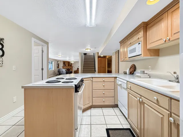 Kitchen featuring light wood-finish cabinetry, a built-in microwave, white electric range, and a double basin sink