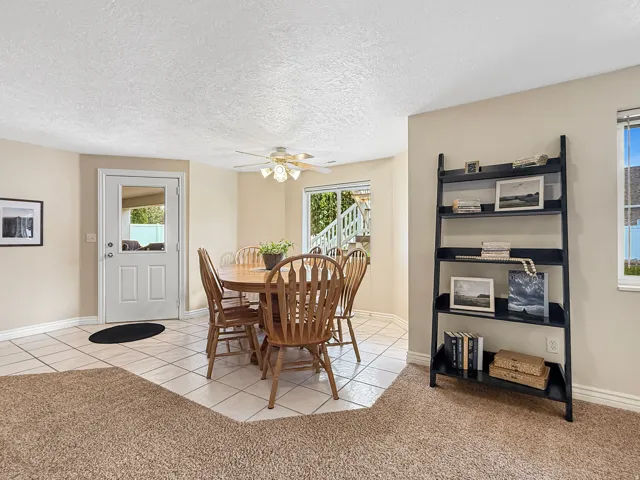 Spacious room featuring ceiling fan, natural light from multiple windows, durable tile flooring, and carpeted area