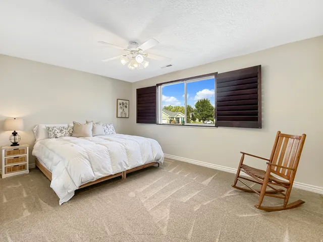 Neutral wall paint, ceiling fan with light fixture, window with louvered shutters, and carpeted flooring