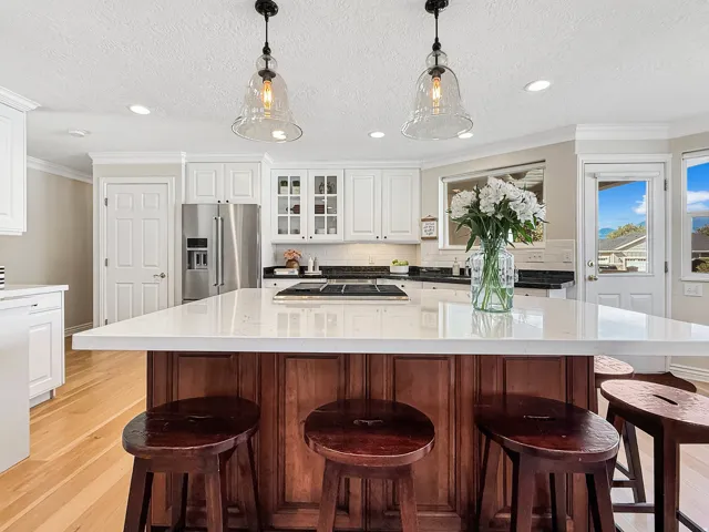 White shaker cabinetry, stainless steel appliances, central island with seating, pendant lighting, and wood-finish flooring