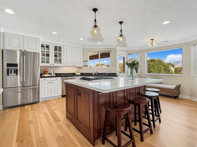 Kitchen featuring a large central island with seating, stainless steel appliances, white perimeter cabinetry, and wood-finish flooring