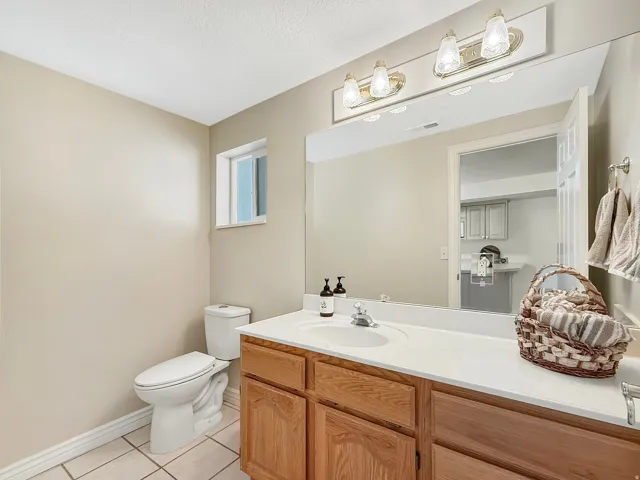 Bathroom featuring a vanity with wood-finish cabinetry, a large wall-mounted mirror, a toilet, a window, and tiled flooring
