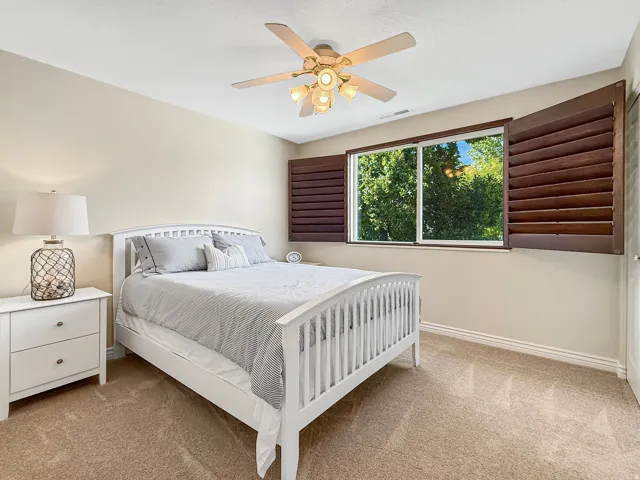 Window with dark wood shutters, ceiling fan with integrated lighting, and neutral carpeting