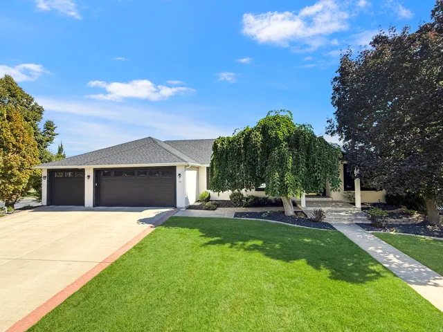 Expansive front lawn with mature trees, a multi-car driveway, and a two-car garage
