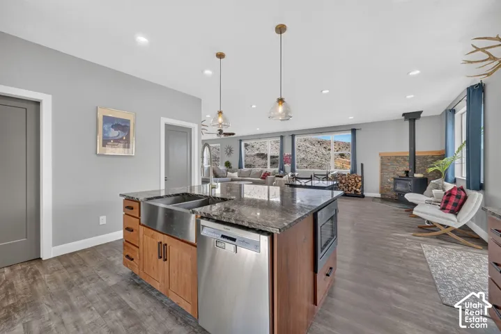 Spacious kitchen island with a farmhouse sink and granite countertop, wood-finish flooring, recessed lighting, and a stone-clad fireplace