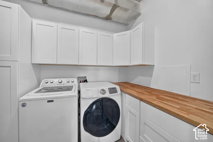 White shaker cabinetry with ample storage, a wood-finish countertop, and utility outlets