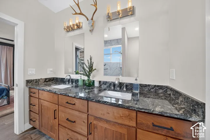 Dual sink vanity with dark wood-finish cabinetry, black hardware, and a dark stone countertop