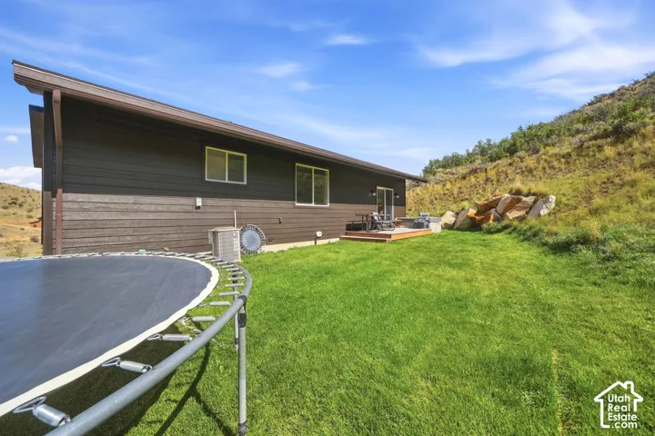 Expansive green lawn with a wood-plank deck, sliding glass door access, and a rock landscaping feature