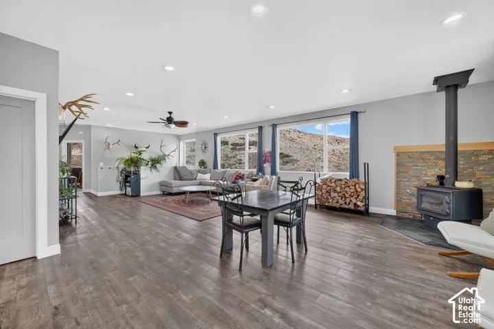 Expansive open-concept living area featuring wood-finish flooring, a stone-faced wood-burning stove, recessed lighting, and multiple windows