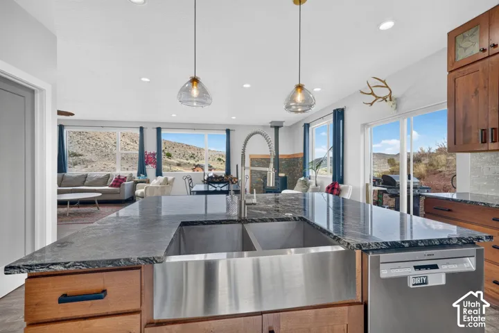 Spacious kitchen island featuring a farmhouse-style sink, stone countertops, and pendant lighting