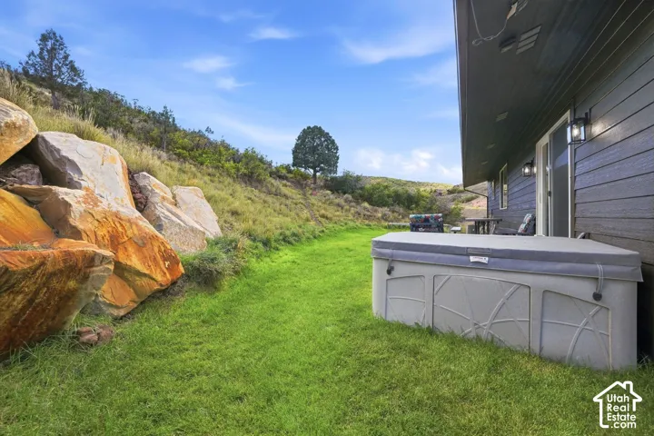 Expansive green lawn with a spa, a sliding glass door, and exterior wall sconces