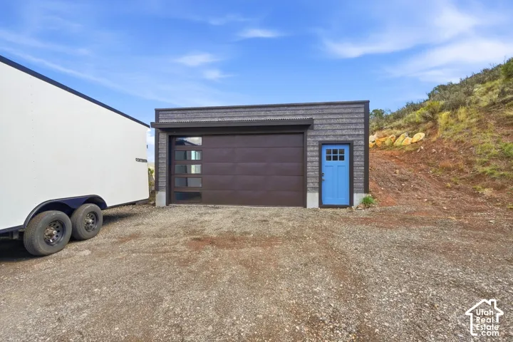 Detached garage with horizontal siding, a brown panel garage door with windows, and an azure pedestrian door