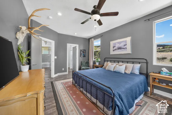 Recessed lighting, sloped ceiling, wood-finish flooring, two large windows, and a ceiling fan with integrated lighting