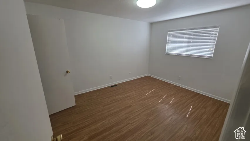 Wood-finish flooring, white walls, and a window with blinds provide a neutral palette