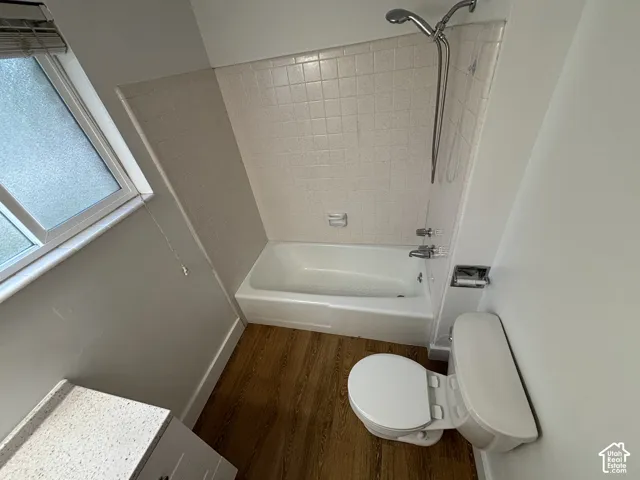 Tub/shower combination with tile surround, wood-finish flooring, and a window with privacy glass