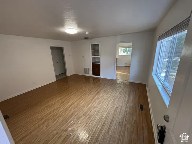 Wood-finish flooring throughout, bright overhead lighting, built-in shelving with cabinetry, and an expansive window with blinds