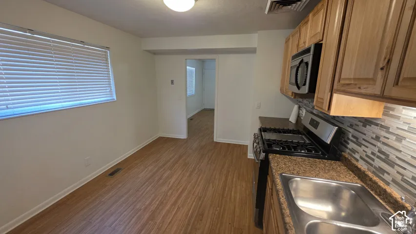 Wood-finish flooring throughout, full kitchen with wood cabinetry, stainless steel double basin sink, and mosaic tile backsplash