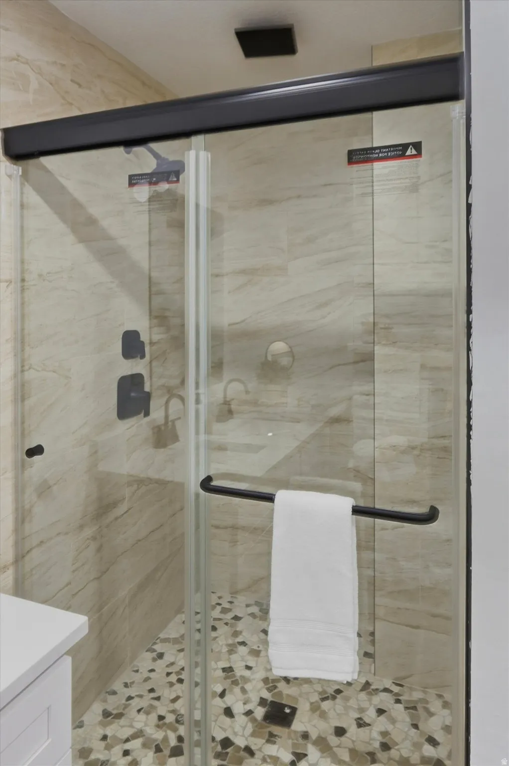 Glass-enclosed shower with a pebble floor, light-toned wall tiling, and matte black fixtures