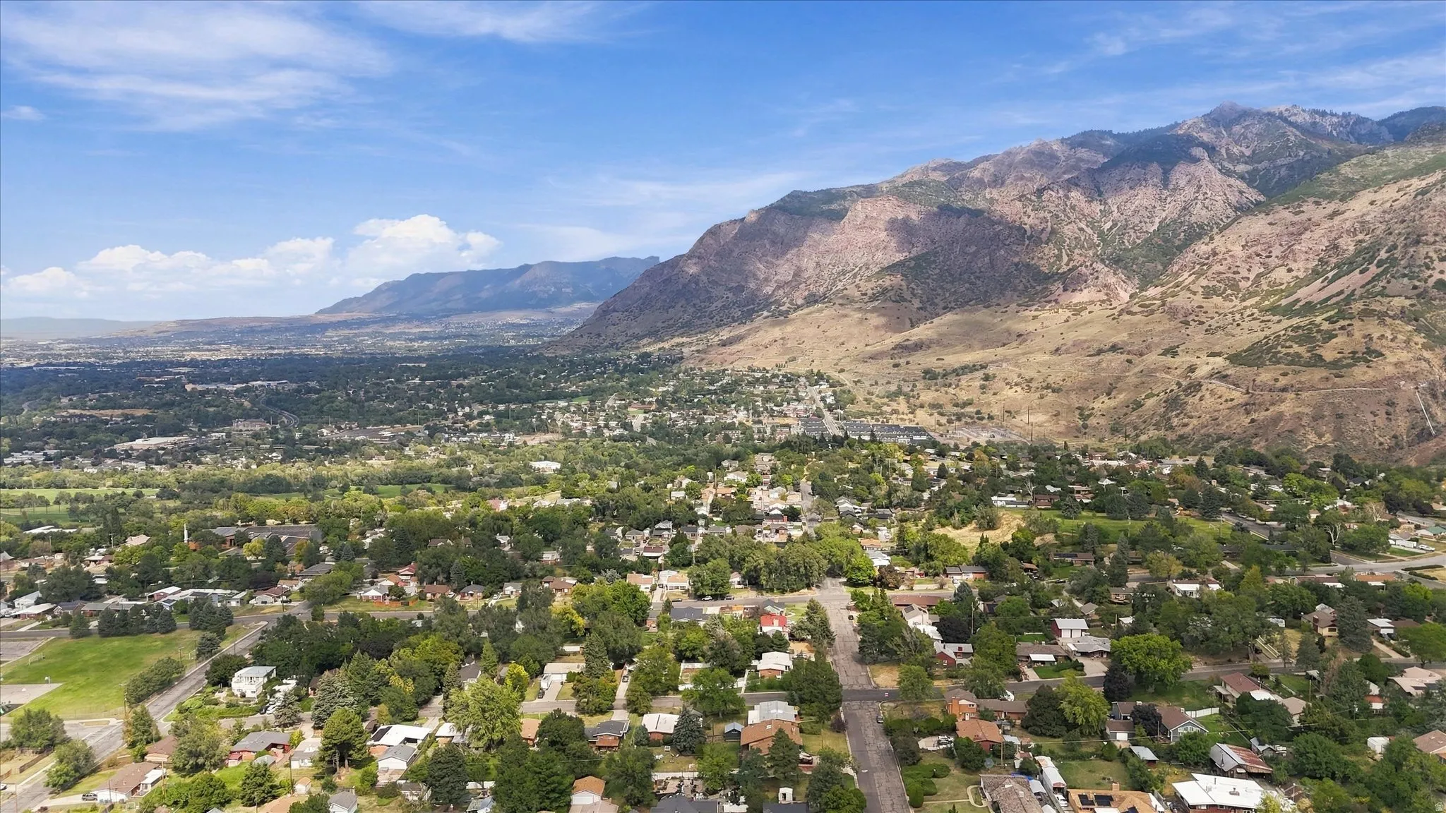 Expansive mountain ranges and distant cities frame the residential area with established trees