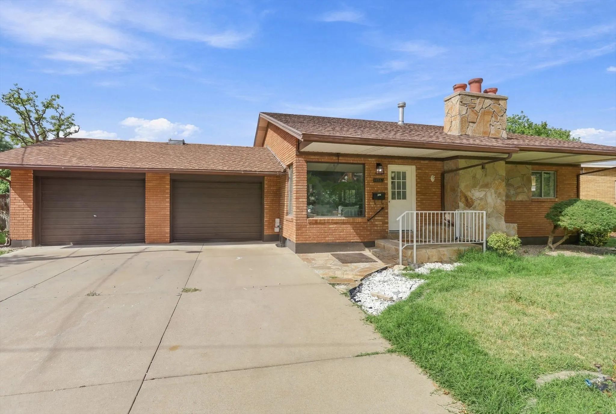 Brick exterior featuring a two-car garage, stone-clad chimney, covered front entry, and a concrete driveway
