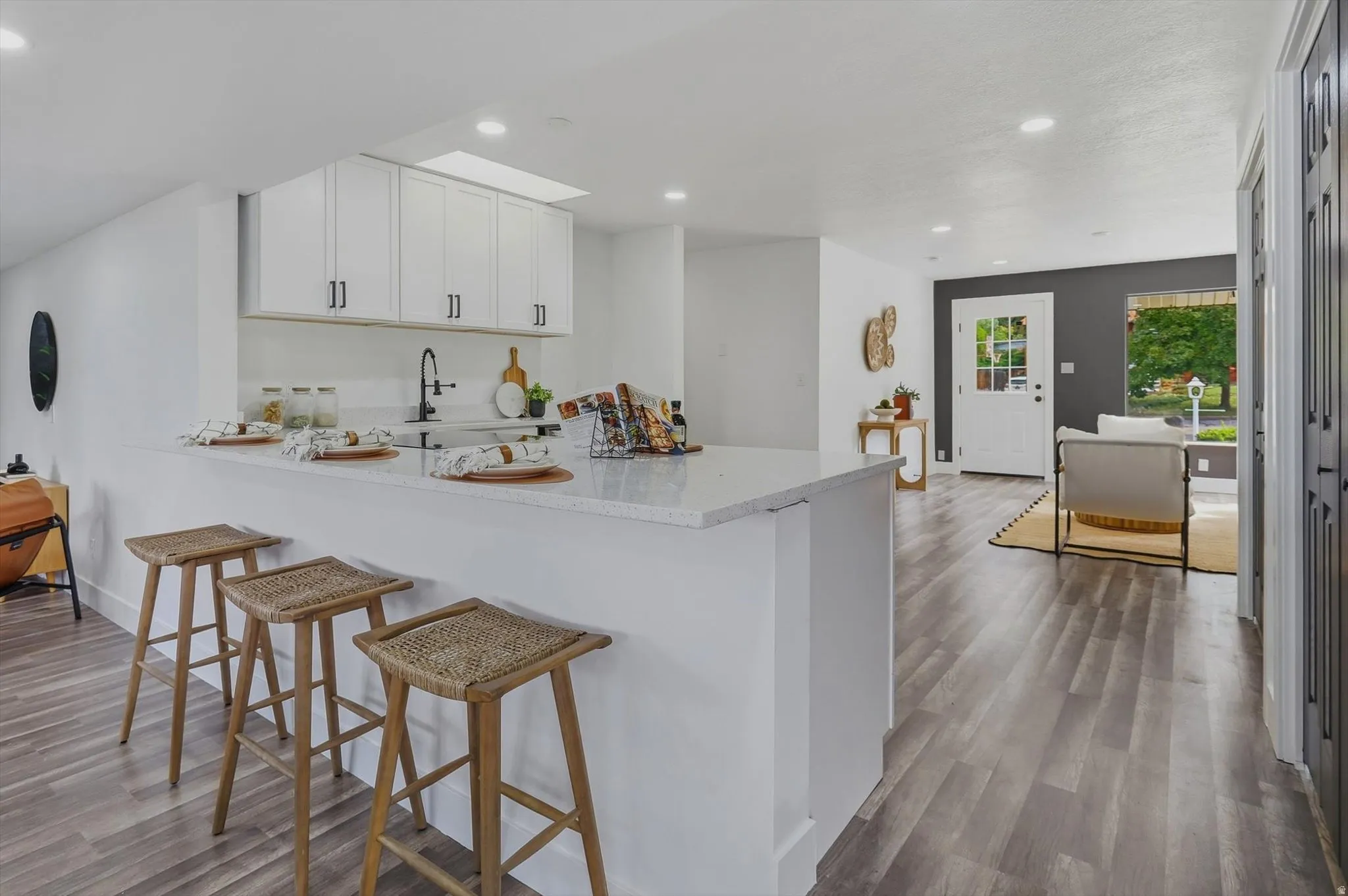 White shaker-style cabinetry with matte black hardware, stone-finish countertops, wood-finish flooring, recessed lighting, and a white paneled front door