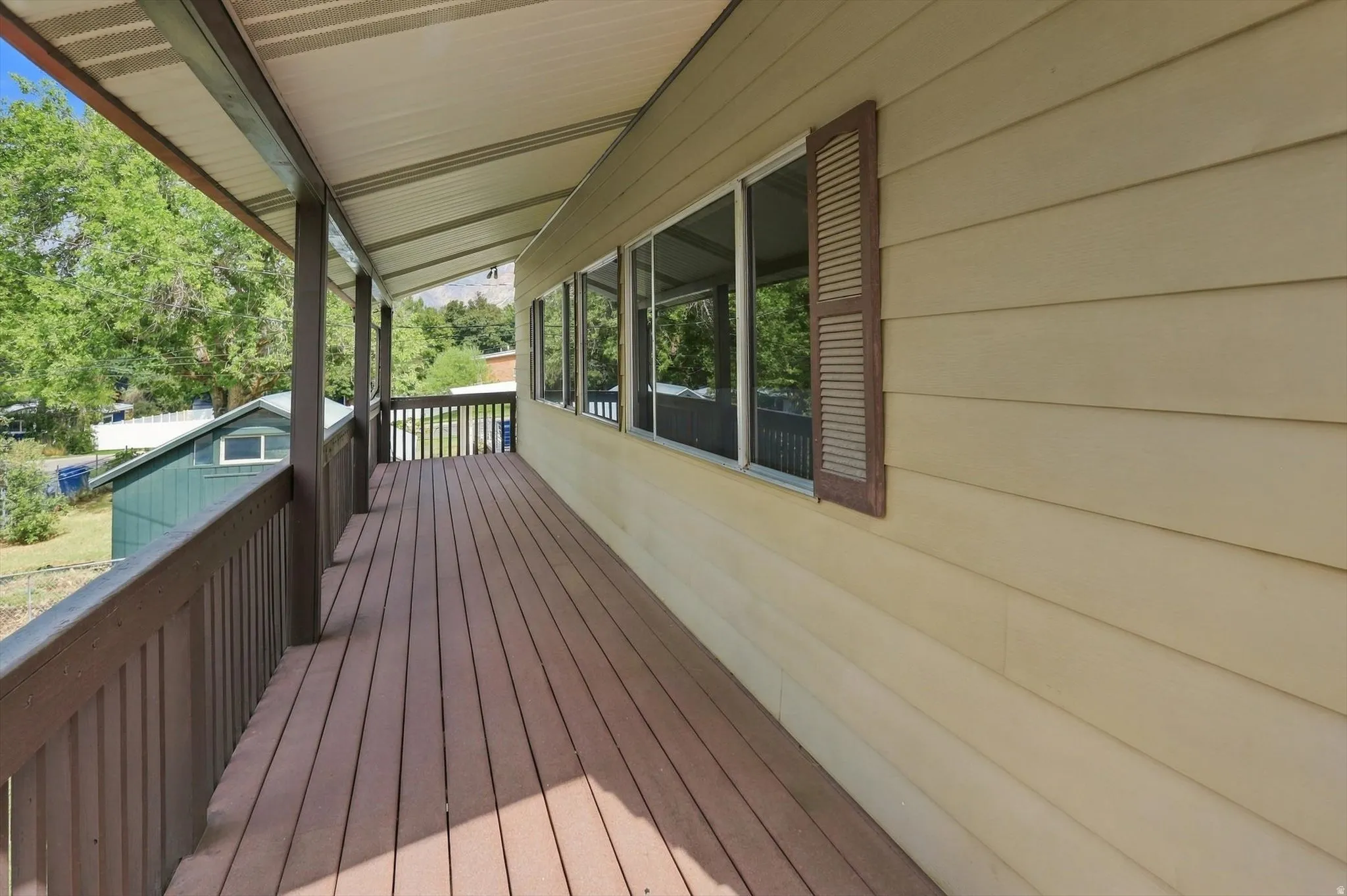 Expansive covered porch featuring wood-finish decking, dark-stained railings, and multiple windows with exterior shutters