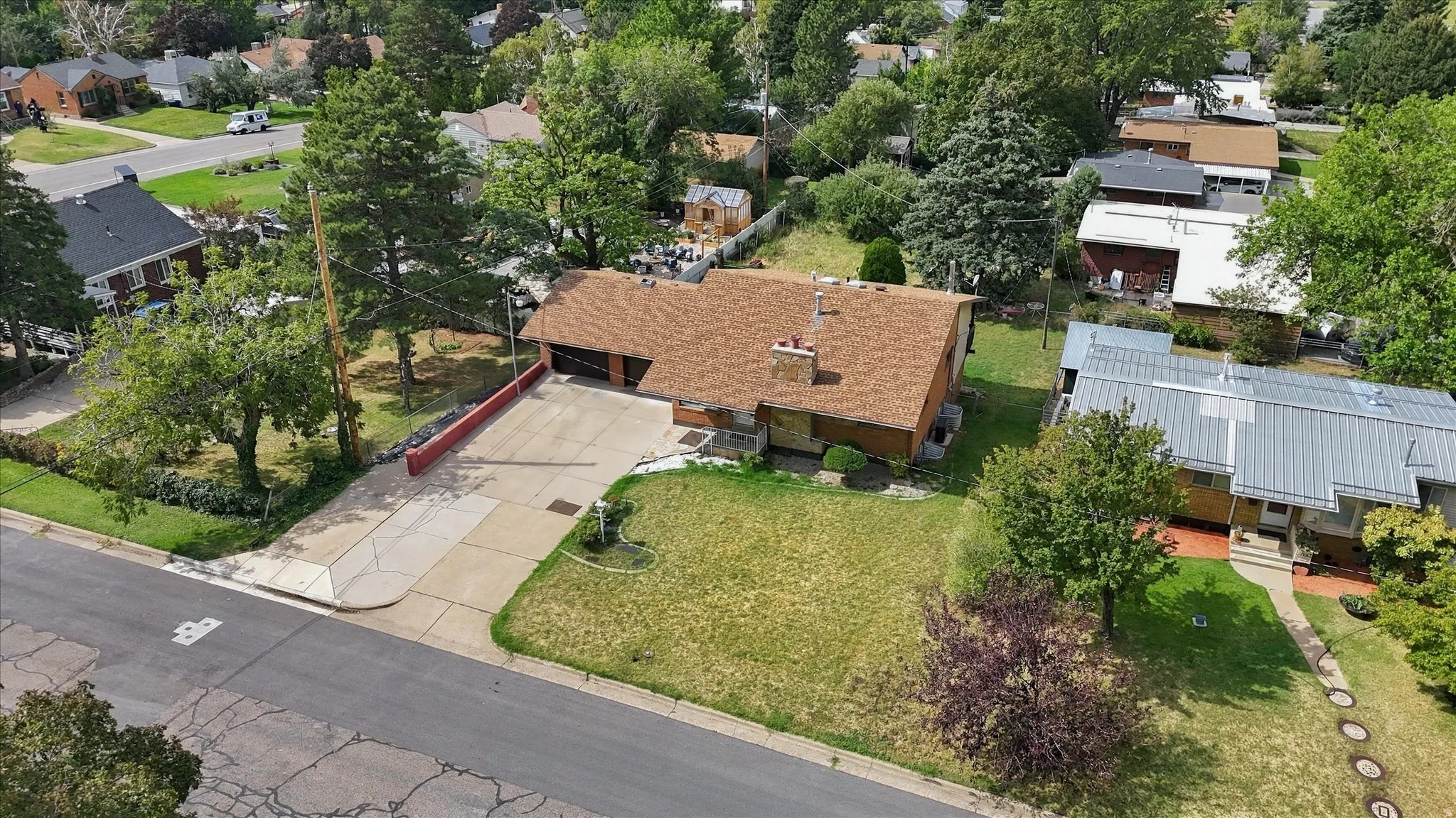 Single-story residence featuring a brown shingle roof, attached garage, and a front lawn with mature trees